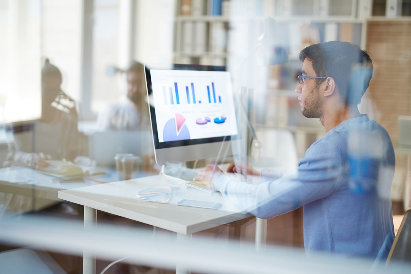 man with glasses at a desk looking at a computer screen
