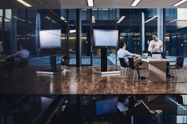 two men sitting with laptops with a TV in the background